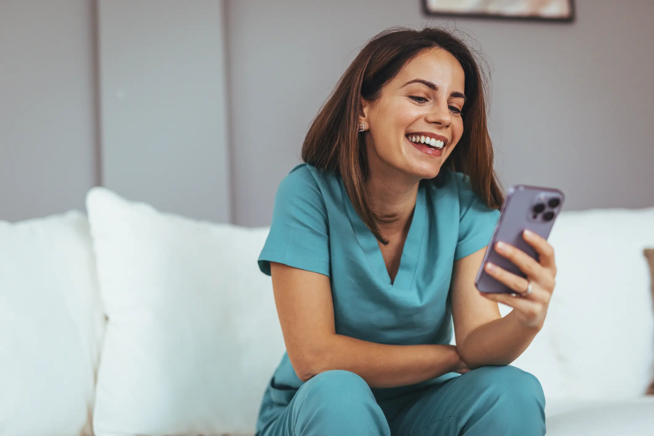 Healthcare professional in teal scrubs smiling while looking at phone